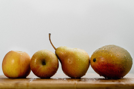 Apples, mango and pear on a wooden table in a rowの写真素材