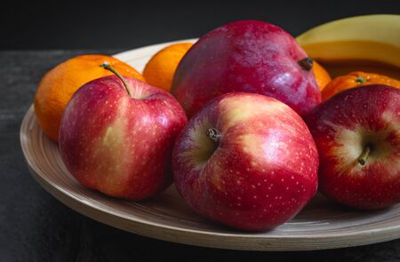 Apples, mandarins, bananas, mango on a plateの写真素材