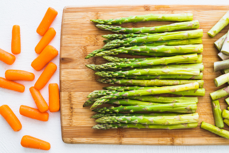 Asparagus and Carrot on a Wooden Chopping Board in White Background, Close Up, Top View. Cooking, Vegetarian, Healthy Eatingの写真素材