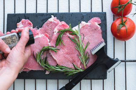 Pork Slices on a Chopping Board, Black Pepper, Rosemary, and Tomatoes. Close Up, Top View. Food Preparation, Recipeの写真素材