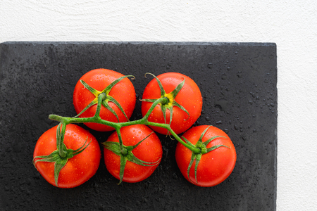 Fresh Red Tomatoes With Drops of Water on a Black Chopping Board in White Background Close Up, Top Viewの写真素材