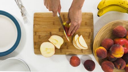 Apple Slices. Woman slicing apple on a wooden cutting board, close up, on white backgroundの写真素材
