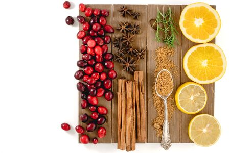 Fresh cranberries, cinnamon, anise, orange, brown sugar, rosemary, and lemon close up, top view on a wooden board, isolated on white backgroundの写真素材