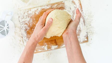 Dough preparation. Woman hands kneading dough in flour on a wooden board. Top view,white background