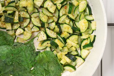 Zucchini and spinach. Roasted sliced zucchini and spinach with some seasoning on a frying pan close up, view from aboveの写真素材