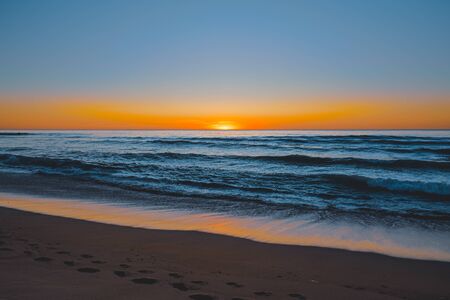 Abstract seascape. Beautiful tropical beach at sunset. Blue ocean, colorful sky, and sun setting down the horizonの写真素材
