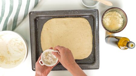 Baking cheese bread step by step. Bread dough on a backing sheet. Close up, top view, woman hands, white background.の写真素材