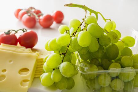 Green grape, cheese, and tomatoes close up on light marble background.の写真素材