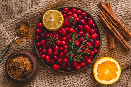 Fresh cranberries, cinnamon, anise, orange, brown sugar, rosemary, and lemon close up, top view on rustic backgroundの写真素材