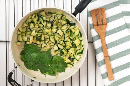 Zucchini and spinach. Roasted sliced zucchini and spinach with some seasoning on a frying pan close up, view from aboveの写真素材