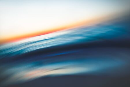 Abstract seascape with blurred panning motion. Before sunrise. Blue sea waves and sun on a horizonの写真素材