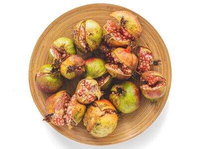 Pomegranates. Cracked ripe organic pomegranates on a wooden plate on white background, directly from aboveの写真素材