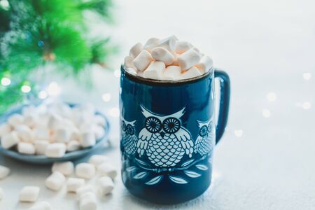 Owl-shaped ceramic mug with marshmallows close up, Christmas tree and Christmas lights background. Holiday greeting card concept, copy spaceの写真素材