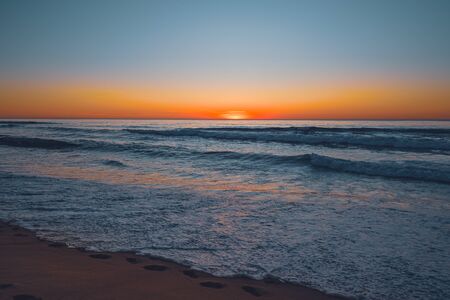 Abstract seascape. Beautiful tropical beach at sunset. Blue ocean, colorful sky, and sun setting down the horizonの写真素材