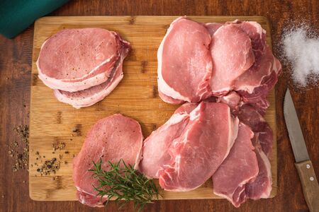 Raw Boneless Pork Loin chops on wooden cutting board with some herbs, salt, and rosemary close up on a wooden rustic background, directly from aboveの写真素材
