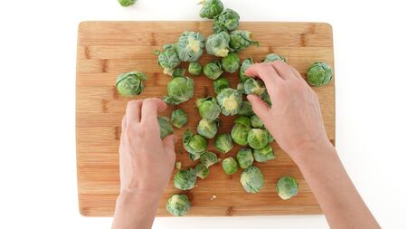 Brussels sprouts on a wooden cutting board, close up on white background, top view, woman handsの写真素材