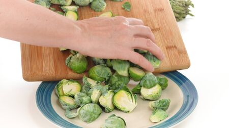 Brussels sprouts. Woman puts Brussels sprouts off cutting board on a plate, close up on white backgroundの写真素材