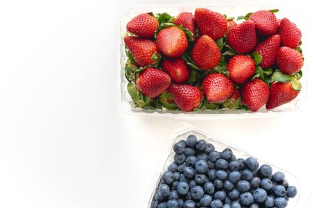 Strawberries and blueberries in plastic container close up on white background, view from aboveの写真素材