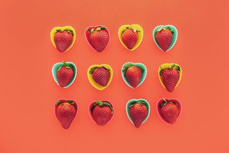 Strawberries in colorful heart shaped plastic molds close up on red background, view from aboveの写真素材