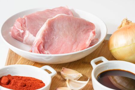 Fresh raw pork meat slices, garlic, onion, soy sauce, and some ingredients on a kitchen table, close up  on white backgroundの写真素材