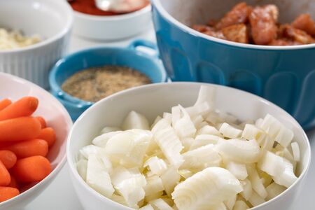 White onion on a plate. Close up of fresh organic chopped onion on a plate among some other ingredients on a kitchen table on white backgroundの写真素材