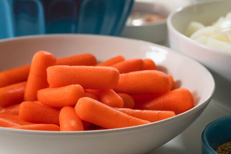 Carrot on a plate. Fresh organic peeled baby carrots close up on a plate among other vegetables on a kitchen table on white backgroundの写真素材