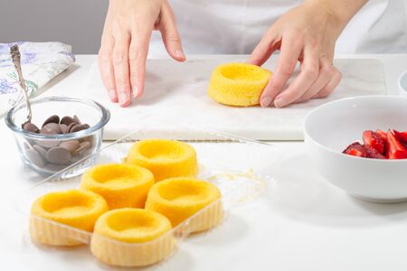 Buiscuit cakes with fresh berries, chocolate, and whipped heavy cream. Woman preparing dessert, mini bisquit cups with strawberries and blueberries,  close up on white backgroundの写真素材
