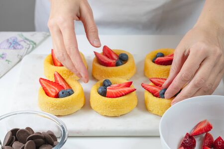 Biscuit cakes with fresh berries, chocolate, and whipped heavy cream. Fresh mini biscuit cups close up on white background, woman handsの写真素材
