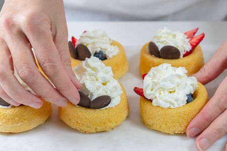 Biscuit cakes with fresh berries, chocolate, and whipped heavy cream. Fresh mini biscuit cups close up on white background, woman handsの写真素材