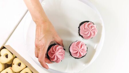 Chocolate cupcakes with raspberry buttercream frosting, and heart shaped cookies close up on white background, top view.の写真素材