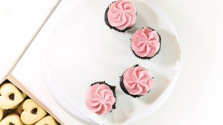 Chocolate cupcakes with raspberry buttercream frosting, and heart shaped cookies close up on white background, top view.の写真素材