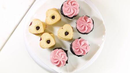 Chocolate cupcakes with raspberry buttercream frosting, and heart shaped cookies close up on white background, top view.の写真素材