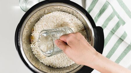 Cooking rice with meat and vegetables  in pressure multi cooker step by step, top view. Pouring water into a pot.の写真素材