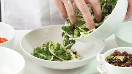 Preparation of vegetable salad step by step. Woman puts fresh green salad mix into a bowl, close up on white backgroundの写真素材