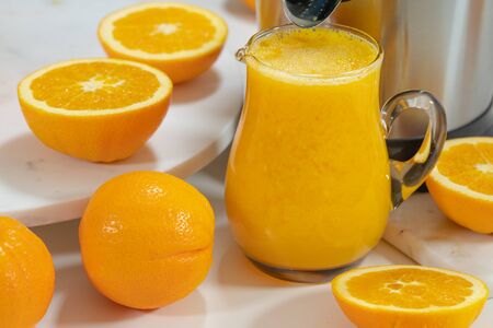 Fresh orange juice in a glass jug and sliced oranges close up. Preparing fresh orange juice using an electric juicerの写真素材