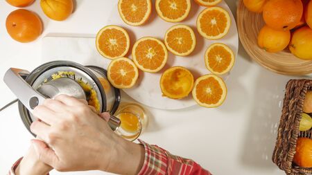 Freshly squeezed orange juice. Caucasian woman squeezing oranges using electric juicer. Close up on white background, view from aboveの写真素材