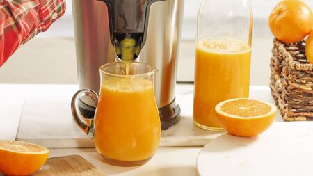 Fresh orange juice in a glass jug close up on white background. Preparing fresh orange juice using an electric juicerの写真素材