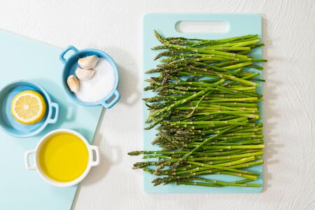 Fresh organic asparagus and some ingredients, as olive oil, salt, garlic, and slice of lemon, on white background, view from above.の写真素材