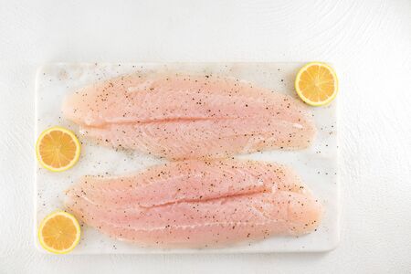 Fresh raw fish fillet. Fillet of sea bass and slices of pink lemon close up on a marble cutting...