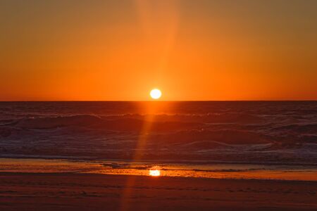 Abstract landscape. Bright red sunset over the sea. Empty beach,visible sun, dramatic seaの写真素材