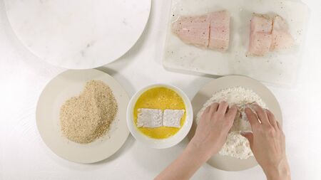 Cooking golden batter deep fried fish fillet. Fresh raw sea bass fillet and some ingredients, as flour, eggs, and and bread crumbs close up on a kitchen table on white background, view from above.の写真素材