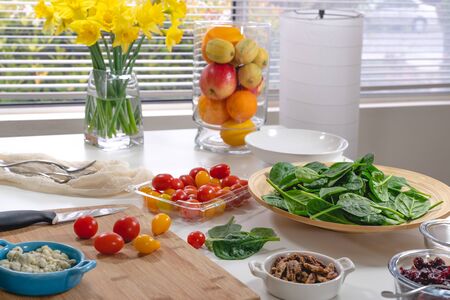 Salad ingredients close up. Spinach, red and yellow tomatoes, blue cheese, pecans, cranberries, and dressing on a kitchen table. Still life, window backgroundの写真素材