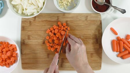Woman chopping carrot on a wooden chopping board, close up on white kitchen table, top viewの写真素材