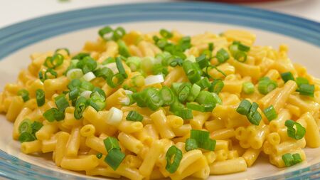 Macaroni and cheese with fresh chopped green onion close up on a plate on a kitchen tableの写真素材
