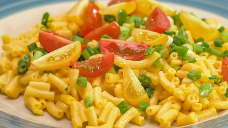 Macaroni and cheese with chopped green onion and sliced cherry tomatoes close up on a plateの写真素材