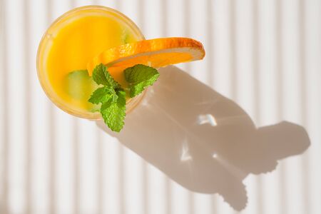 Glass of orange juice with mint leaves and slice of orange close up in bright sunshine from the window, view from aboveの写真素材