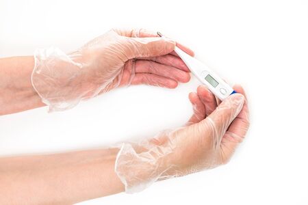 Female hands wearing in vinyl gloves holding a digital thermometer. Close up shot, isolated on white backgroundの写真素材