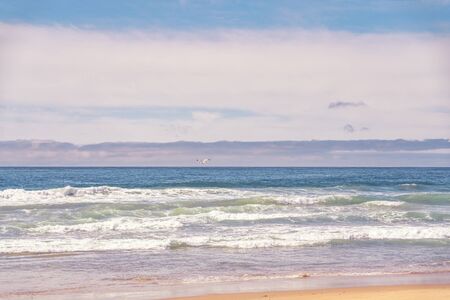 Seascape in light blue and pink colors. Beautiful ocean, cloudy sky, and seagullの写真素材
