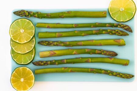 Asparagus and sliced lemon close up on blue serving board on white background, view from aboveの写真素材