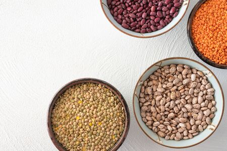 Red lentils, green lentils, small red beans, and pinto beans in a bowls close up on white background, view from above with copy spaceの写真素材
